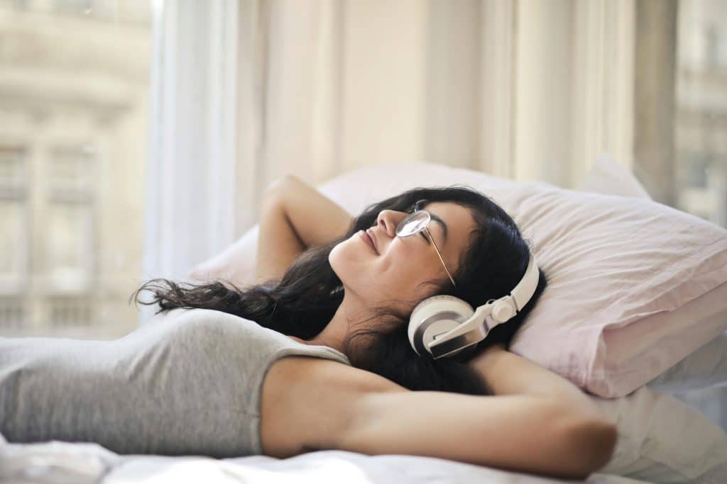 Frau auf ihrem Bett, die Musik auf Spotify hört.
